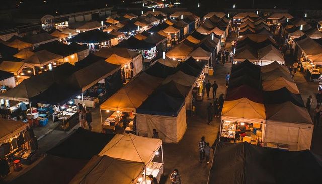 Night market rows of lit pop-up tents and bustling aisle with vendors and evening shoppers