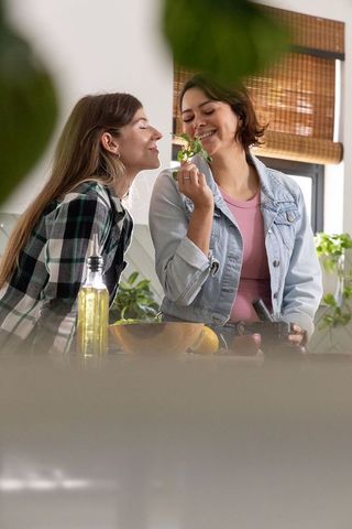 Diverse female partners preparing fresh herbs with mortar and pestle in sunlit kitchen