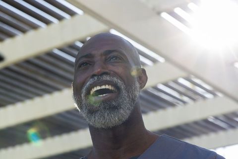 Joyful african american senior man laughing under sunlit pergola, outdoor portrait