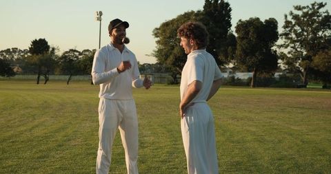 Two cricketers discussing tactics while tossing leather ball on sunlit cricket field