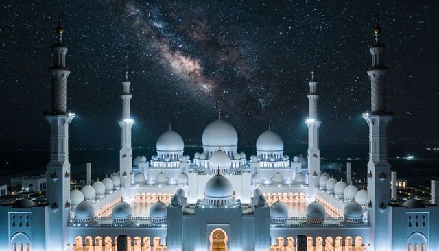 Milky way over illuminated grand mosque at night with symmetrical domes and minarets
