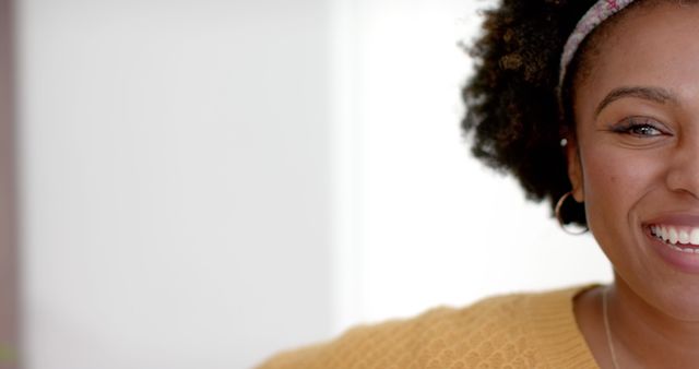 This close-up of a cheerful African American woman wearing a yellow sweater and headband captures genuine joy and positivity. Ideal for advertising happiness, positive vibes, and inclusive representation in lifestyles or casual contexts.
