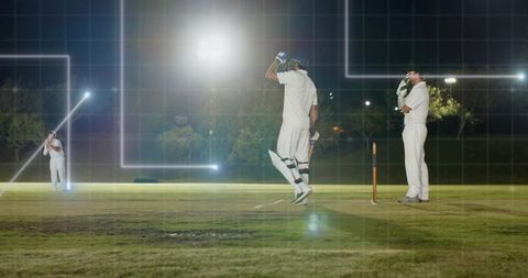 Night cricket batter adjusting helmet on floodlit pitch with wicket and teammates