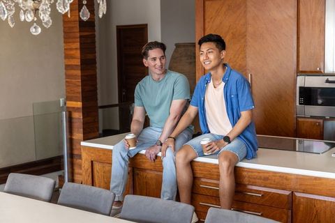 Caucasian and asian friends chatting while sipping coffee on wooden kitchen island