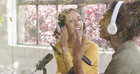 Female podcast co-hosts recording lively conversation in sunlit studio with headphones