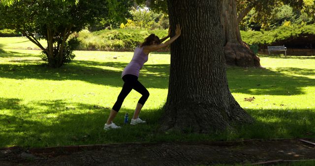 Runner stretching her legs leaning against tree on a sunny day
