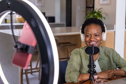 African american woman recording podcast at kitchen table with headset and ring light mic