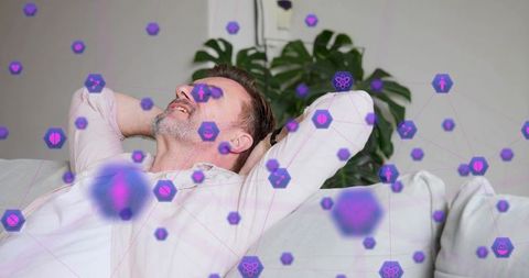 Relaxing middle-aged man on sofa with purple digital wellness network overlay