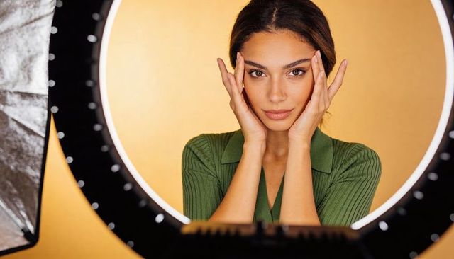 Glam portrait: woman posing with ring light framing face on warm golden backdrop