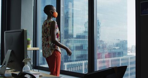 Professional Woman in Mask Observing Cityscape from Office Window