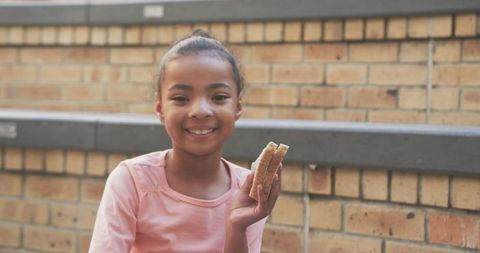 Smiling child eating sandwich on schoolyard bench