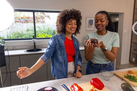Diverse friends filming cooking tutorial chopping red bell peppers in bright home kitchen