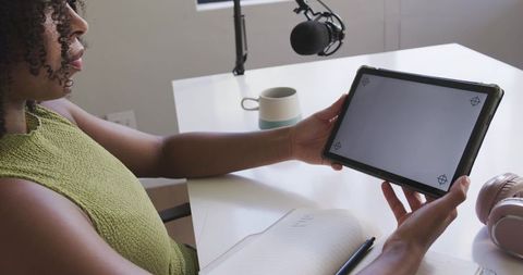 African american woman holding tablet and planning podcast content in home workspace