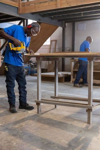 African american men working in carpentry workshop cutting lumber with jigsaw, teamwork