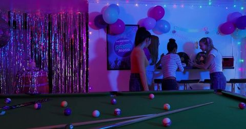 Neon-lit birthday party with friends gathered around pool table, disco bar and balloons