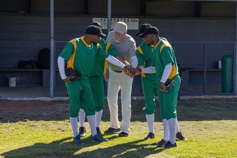 Coach rallying baseball players in dugout huddle before game, planning strategy on field
