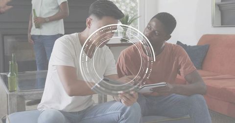 Young men collaborating over tablet with futuristic HUD overlay in casual living room