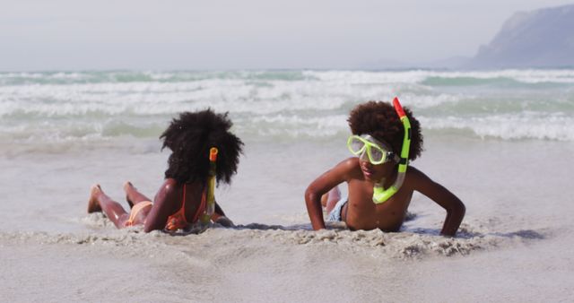 Two African American children are enjoying a day at the beach, lying in the sand with snorkeling gear. Bright smiles and playful energy radiate from the scene, set against the backdrop of waves approaching the shore. Perfect for summer vacation themes, family beach trips, outdoor activities, and illustrations of joyful childhood moments.
