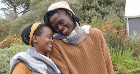 African American couple sharing tender moment in garden wearing cozy knit scarves and beanie