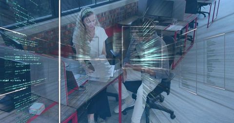 Collaborating professionals reviewing code at open-plan office desk with laptop tablet