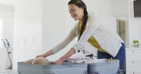 Mid-adult korean woman packing suitcase in bright modern bedroom preparing for travel