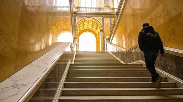 Man climbing grand marble staircase toward gilded arch in historic museum interior