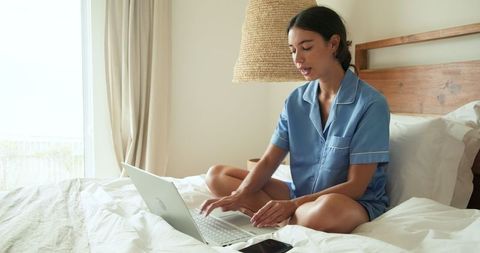 Woman in Pajamas Working on Laptop in Cozy Bedroom Ambiance