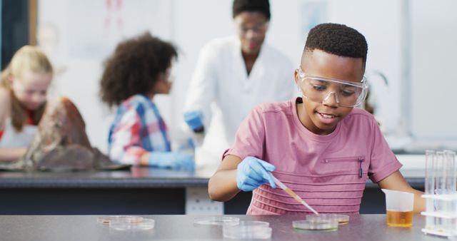 Boy conducting science experiments in modern laboratory, wearing goggles and gloves, using pipette and petri dishes. Other students in background. Ideal for promoting STEM education, school programs, scientific research, and learning environments. Perfect for educational materials, school websites, and scientific publications.