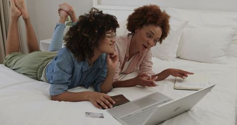 African American women planning trip using laptop and passport on cozy bed