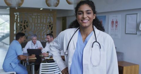Smiling female doctor wearing stethoscope in hospital lounge with collaborating medical team