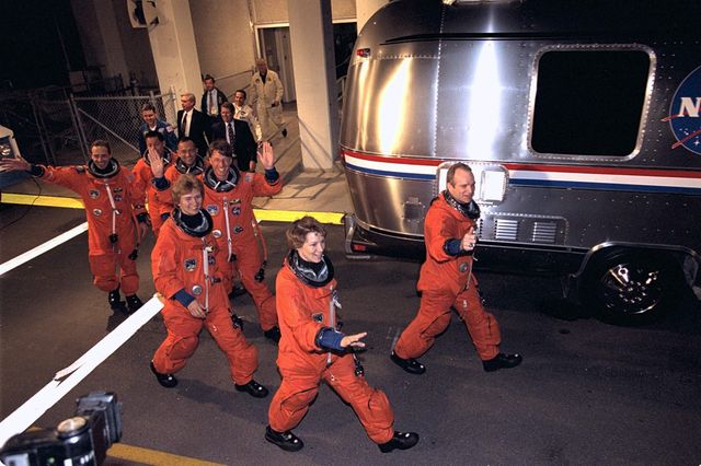 Astronauts from Mission STS-84 are walking exuberantly towards the launch site to board the Space Shuttle Atlantis, which will dock with the Russian Mir Space Station. This mission marks the sixth docking with Mir. Suitable for documenting historical space missions, space exploration articles, and commemorating NASA's missions.
