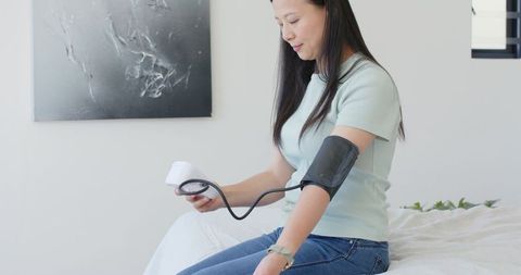 East asian woman measuring blood pressure at home with digital upper-arm cuff