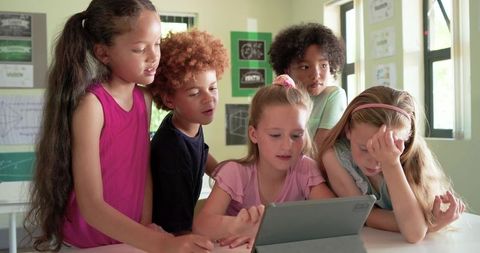 Diverse schoolchildren collaborating on tablet in bright classroom, teamwork and digital learning