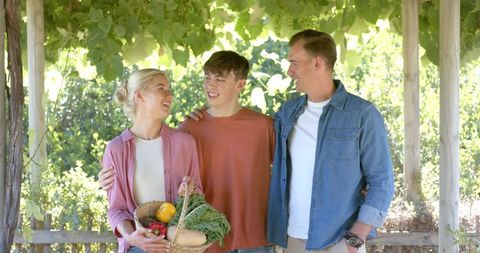 Family harvesting fresh vegetables under pergola smiling parents and teen son