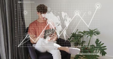 Young man sitting using smartphone with global analytics overlay in modern living room