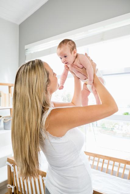 Mother holding and lifting her baby in a modern, bright nursery with natural light. Perfect for use in parenting blogs, family-oriented advertisements, or articles on motherhood and bonding.