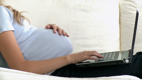 Pregnant Woman Relaxing on Sofa Using Laptop at Home