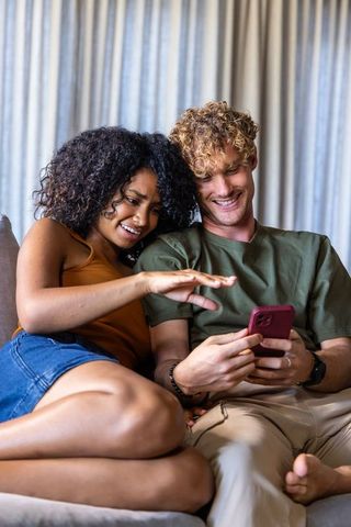Cozy couple sharing smartphone on sofa, laughing and relaxing in modern home