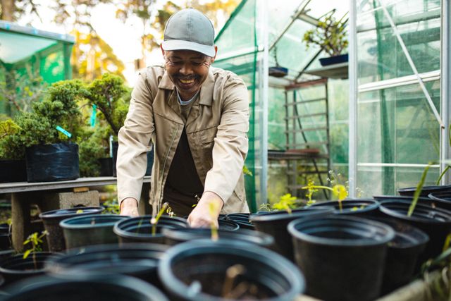 African American male gardener smiling while preparing pots for planting in a bonsai nursery. Ideal for content related to gardening, horticulture, small business, independent work, and nature. Can be used in articles, blogs, and advertisements promoting gardening services, plant nurseries, and sustainable agriculture.