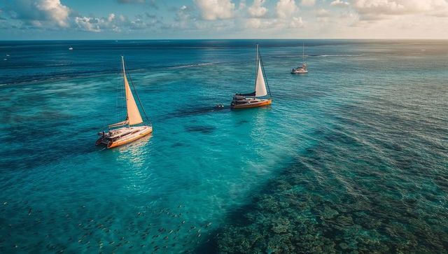 Gliding catamarans over turquoise coral reef at golden hour — aerial seascape