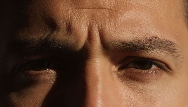 Furrowing brow close-up showing skin texture, pores and shadow on adult male face