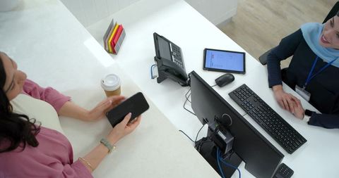 Friendly front desk exchange: female customer holding smartphone, receptionist smiling