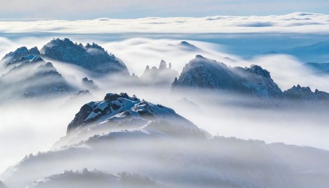 Snowy alpine ridge rising through sea of clouds with jagged spires and misty peaks