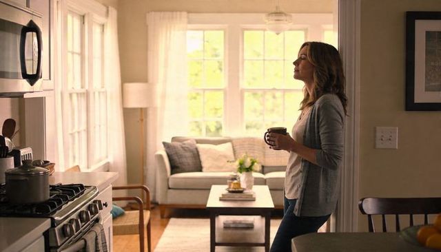 Woman holding coffee gazing out window in cozy open kitchen and sunlit living room