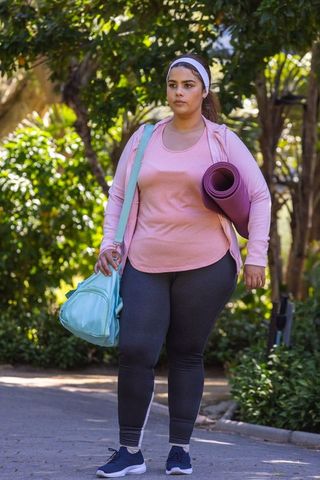 African american woman walking to yoga carrying mat and duffel in sunlit park