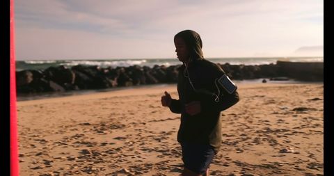 Determined Runner Jogging on Beach with Ocean Waves Behind