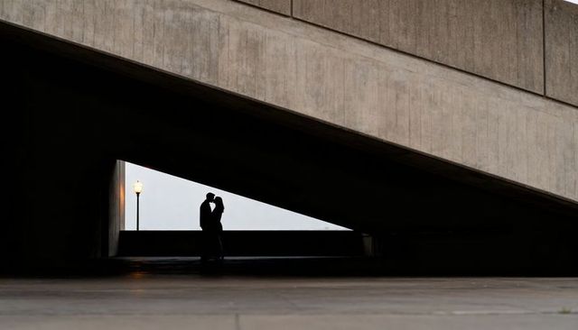 Silhouetted couple kissing beneath geometric overpass with glowing streetlamp, urban romance