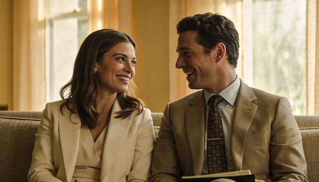 Smiling professional couple sharing warm moment on beige sofa in sunlit office lounge