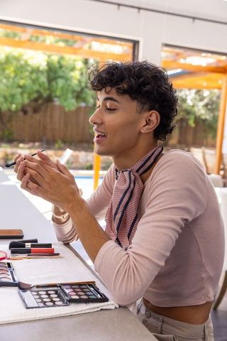 Man perfecting makeup skills with eyeshadow and brush on patio