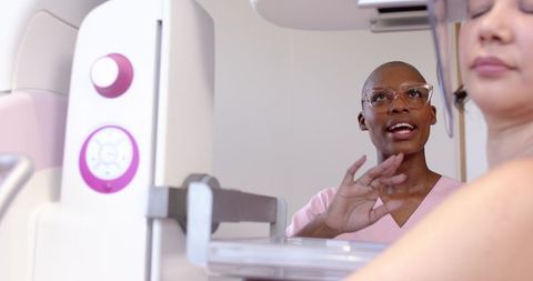 Mammography technician guiding patient during breast screening procedure in clinic